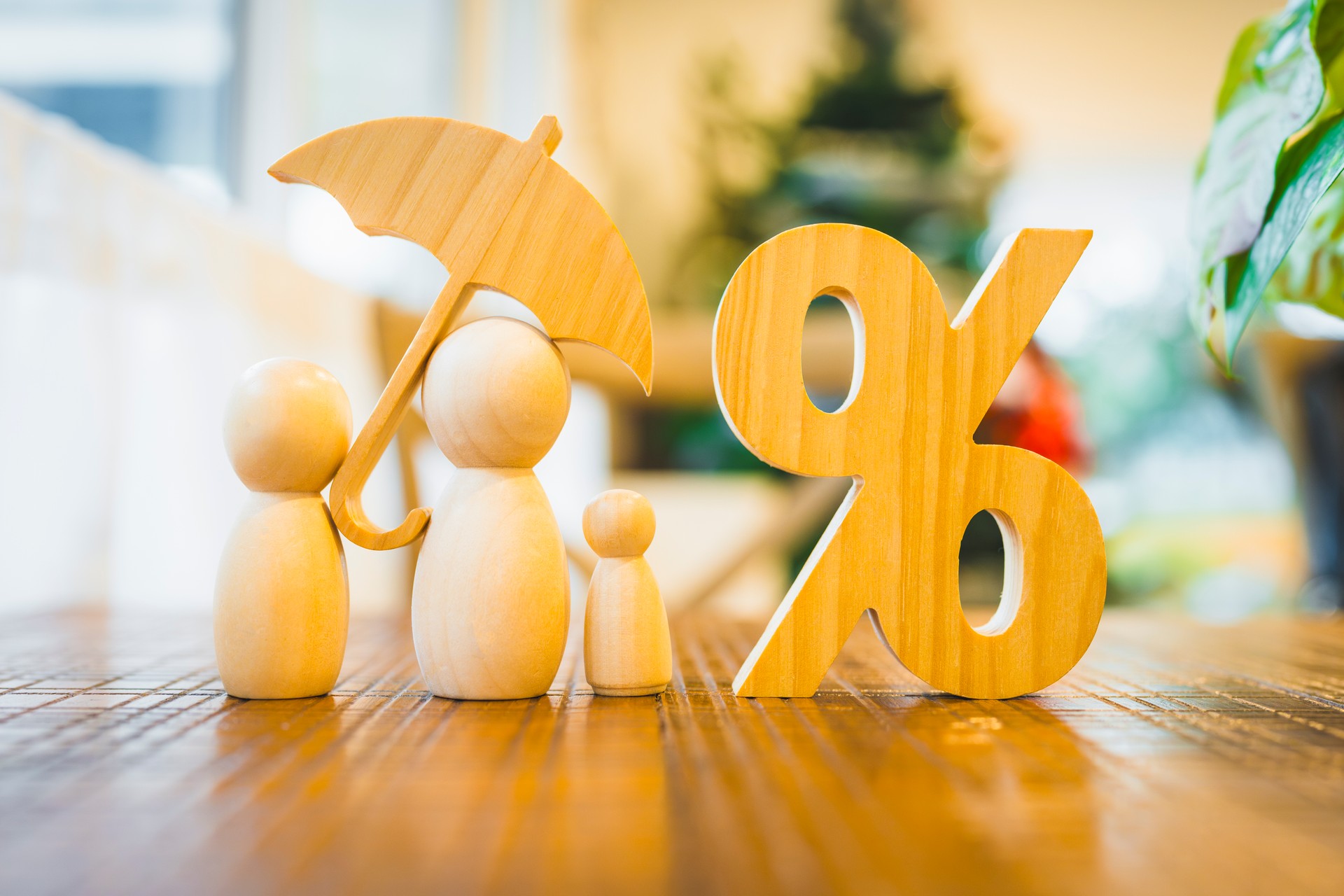 A picture of a wooden model and a family of parents and children holding an umbrella biting a percentage symbol. The picture is a picture with a concept about insurance planning.